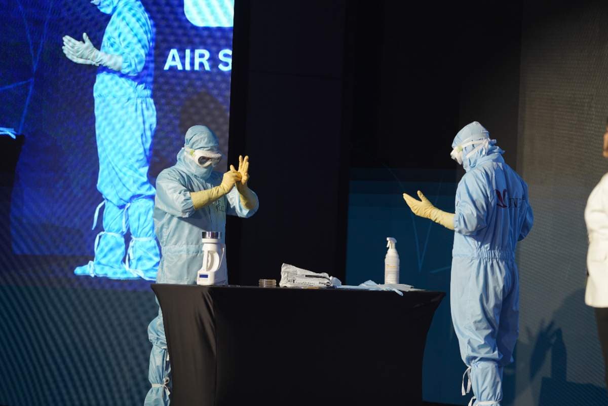 Two operators in full cleanroom gowns demonstrating aseptic gowning live on stage
